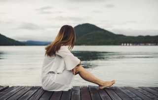 Lonely woman sitting on wooden pier and looking at the lake